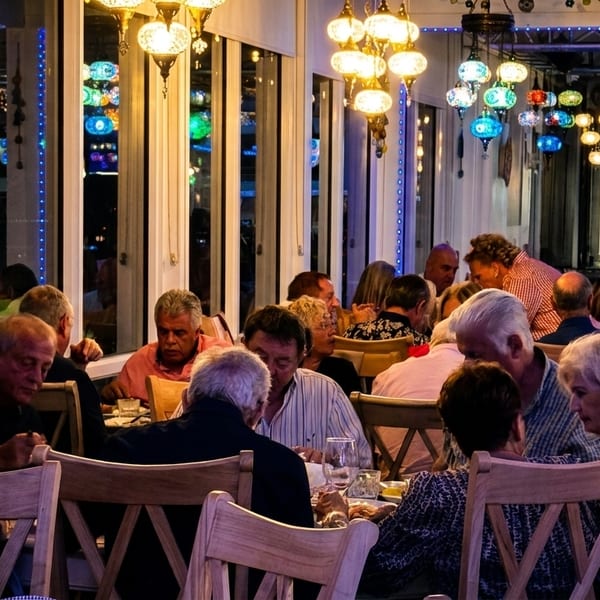 Diners seated at tables in a restaurant with colorful, ornate hanging lamps illuminating the space.
