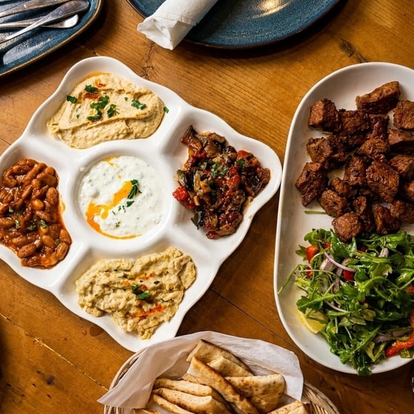 Overhead view of a wooden table laden with a mezze platter, meat, salad, and pita bread.