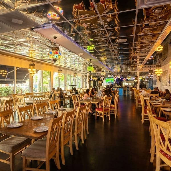 Spacious restaurant interior with wooden tables, chairs, ornate hanging lamps, and a mirrored ceiling.