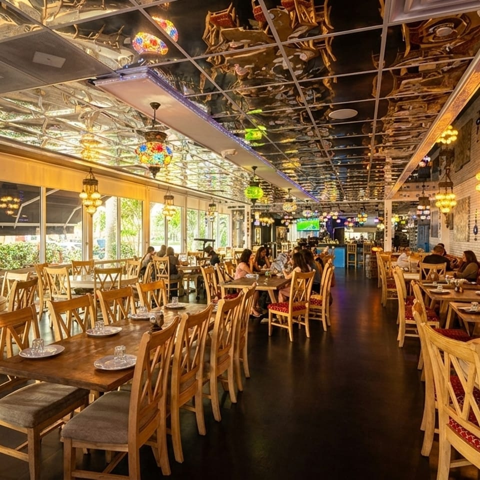 Spacious restaurant interior with wooden tables, chairs, ornate hanging lamps, and a mirrored ceiling.