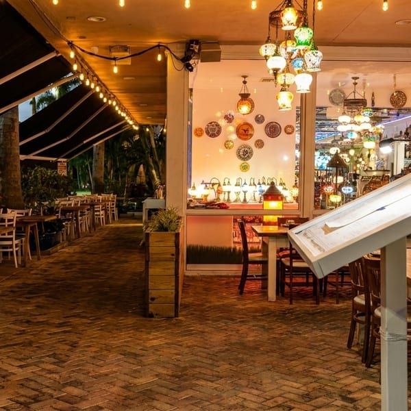 An outdoor patio dining area with string lights and a brightly lit interior with decorative lamps.